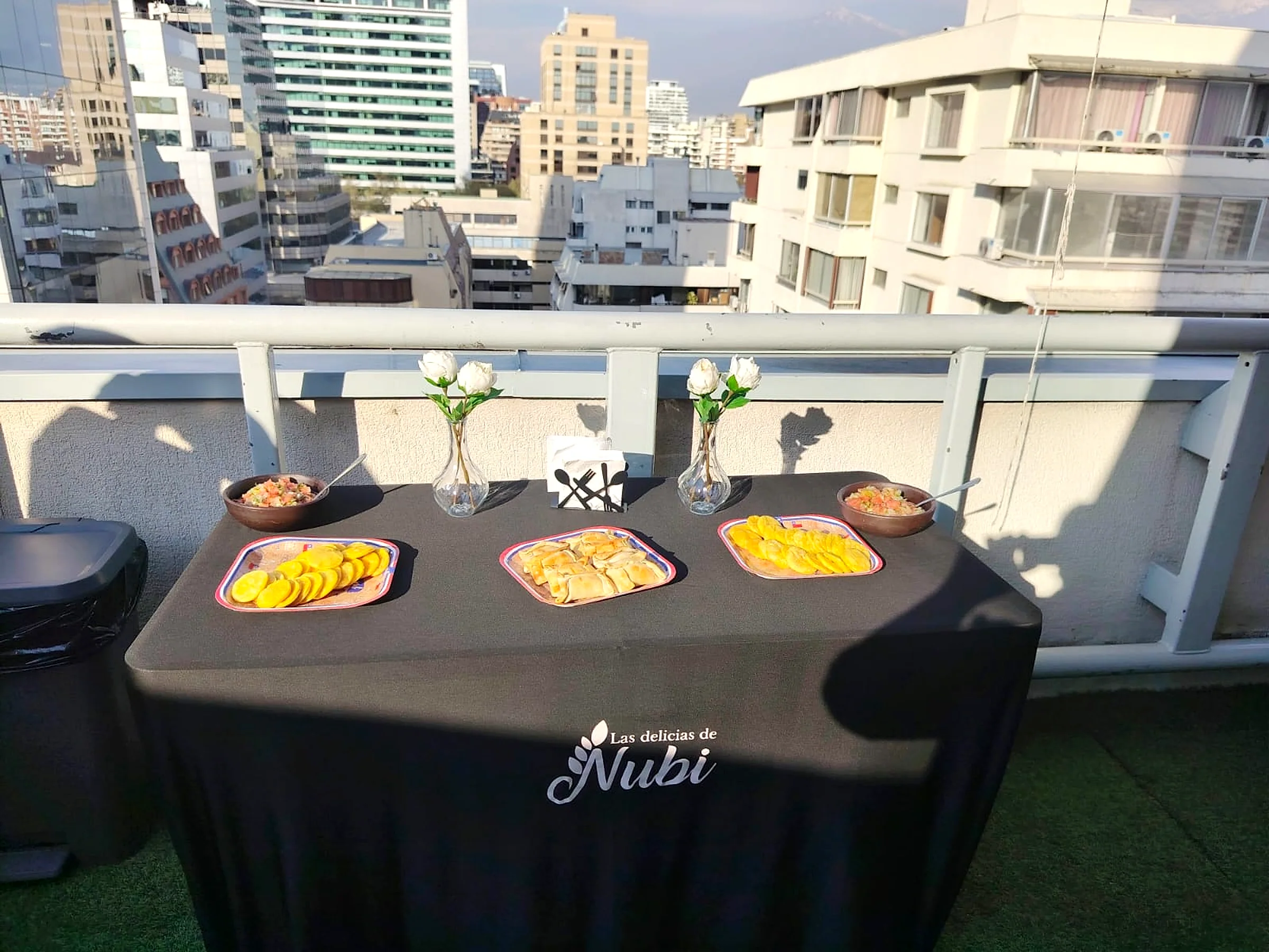 Mesa de coffee break de Las delicias de Nubi montada en una terraza, con mantel de la marca